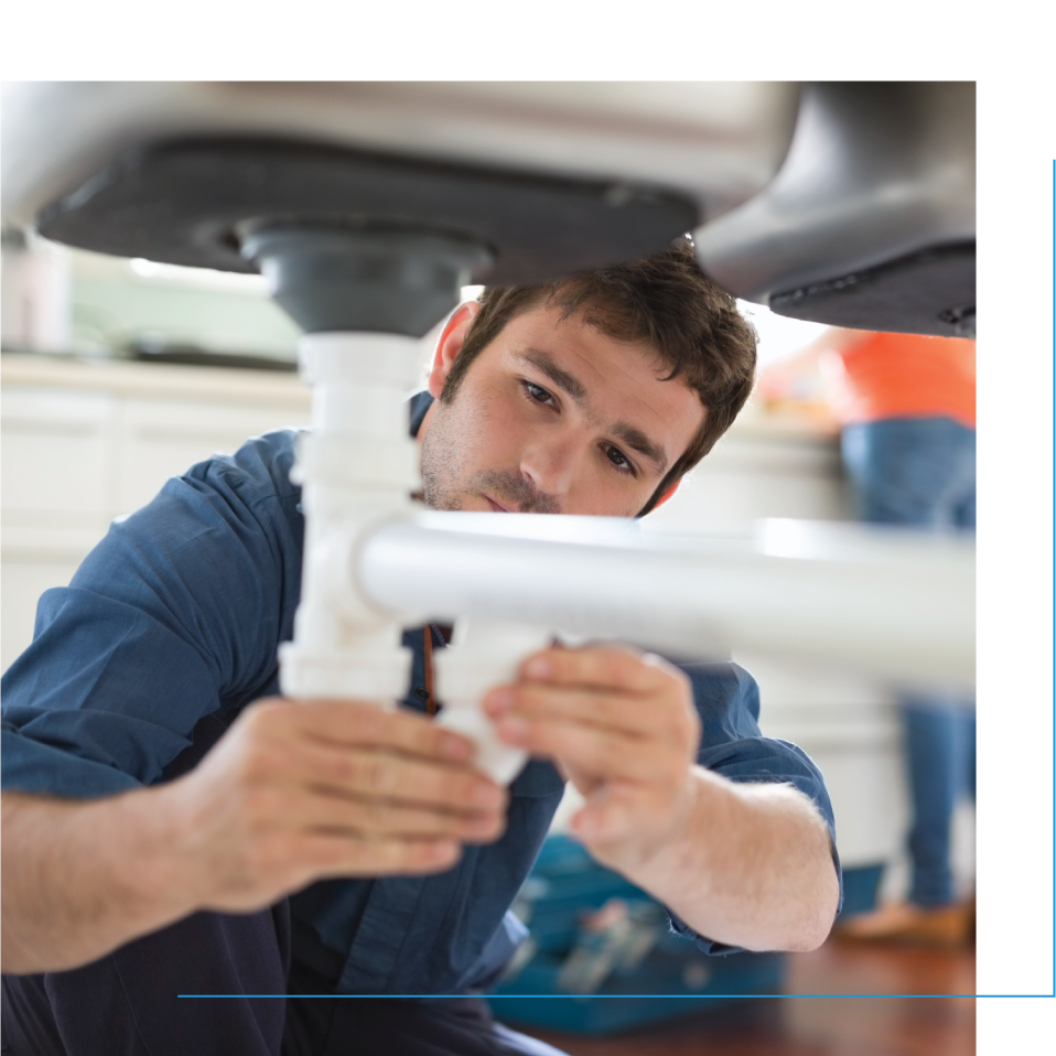 A male plumber working on the pipes under a sink